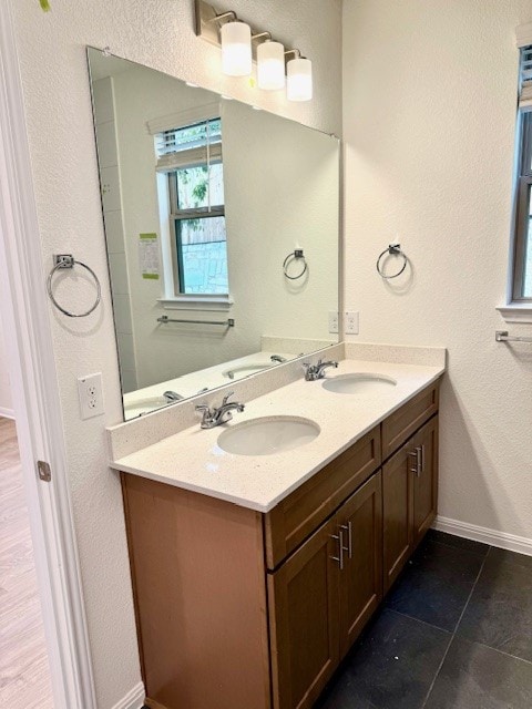 full bath with double vanity, baseboards, and a sink