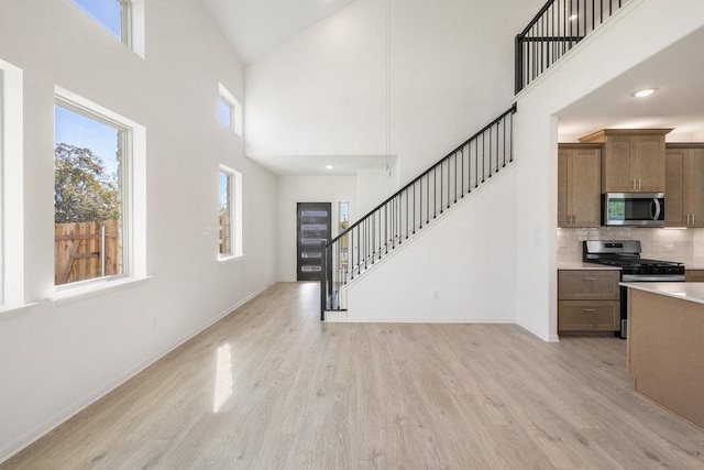 interior space with light wood-type flooring, stairs, baseboards, and a high ceiling