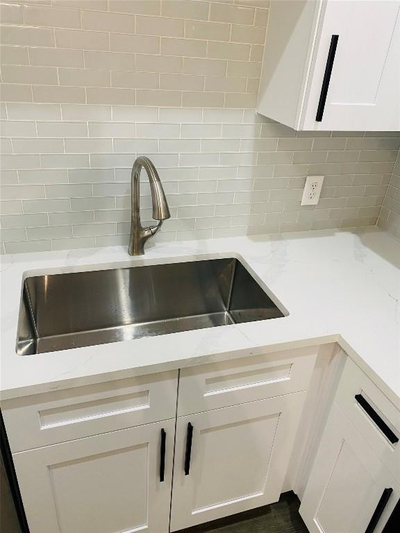 room details featuring tasteful backsplash, a sink, light stone counters, and white cabinets