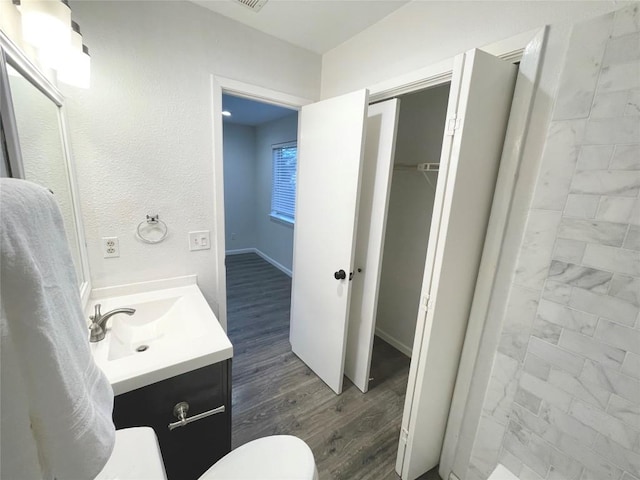 bathroom with toilet, vanity, wood finished floors, tiled shower, and baseboards