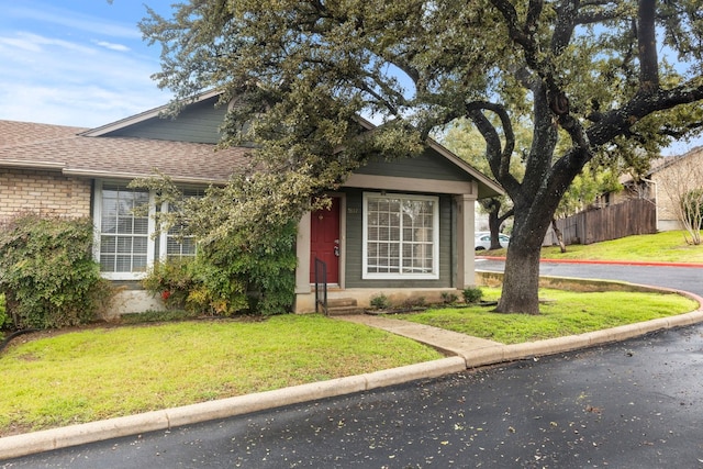 view of front of home featuring a shingled roof, fence, and a front lawn