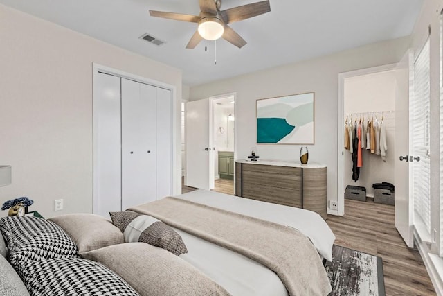 bedroom featuring a closet, visible vents, a spacious closet, light wood-style floors, and ensuite bath