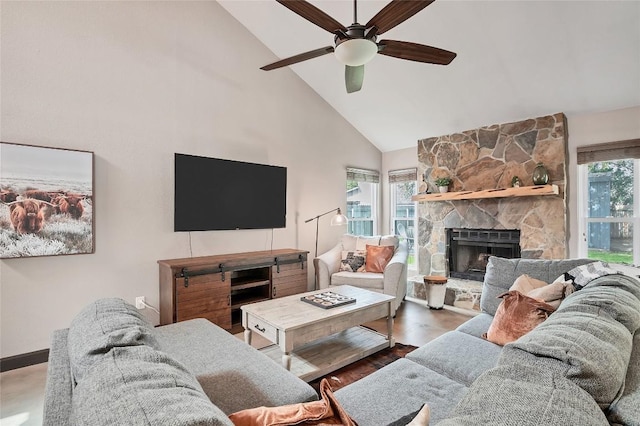 living room with high vaulted ceiling, a stone fireplace, wood finished floors, and a wealth of natural light