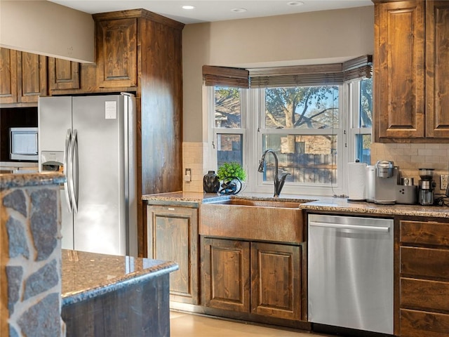 kitchen with light stone countertops, backsplash, stainless steel appliances, and a sink