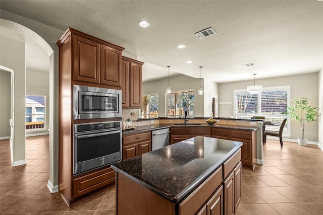 kitchen with stainless steel appliances, a peninsula, dark tile patterned floors, a sink, and visible vents