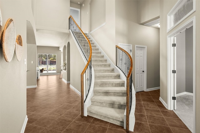 staircase featuring arched walkways, tile patterned flooring, a high ceiling, visible vents, and baseboards