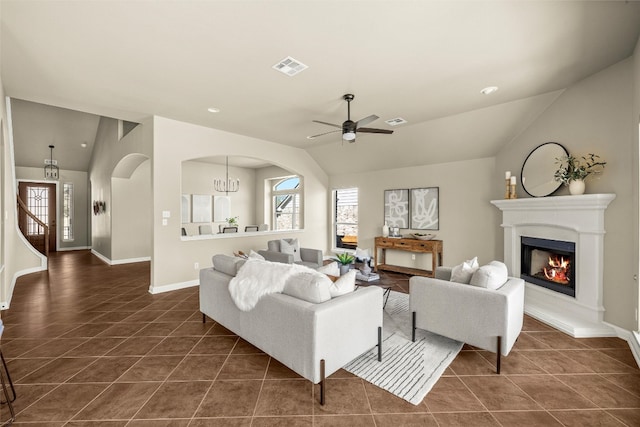 living area featuring lofted ceiling, dark tile patterned floors, a glass covered fireplace, and visible vents