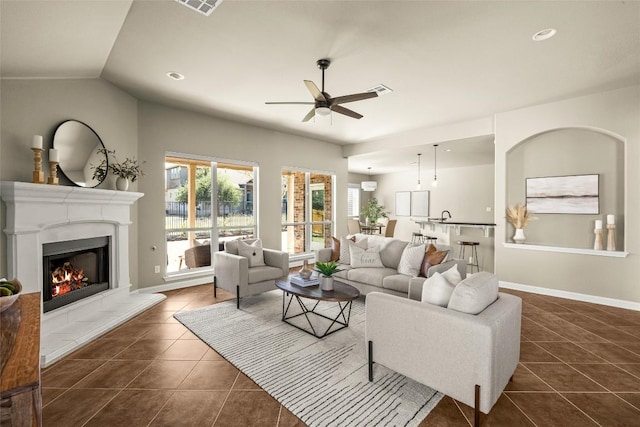 living area featuring dark tile patterned floors, vaulted ceiling, ceiling fan, a lit fireplace, and baseboards