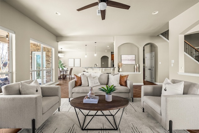 living area with arched walkways, a ceiling fan, tile patterned flooring, stairs, and recessed lighting