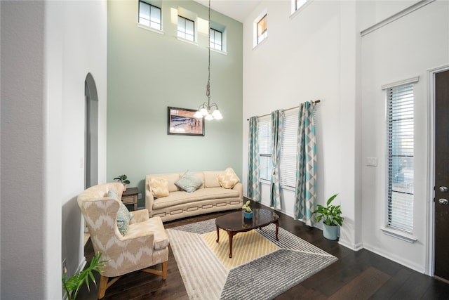 living area with baseboards, arched walkways, dark wood-type flooring, a high ceiling, and a chandelier