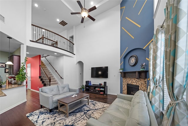 living area with arched walkways, ceiling fan, a tile fireplace, dark wood-style flooring, and stairway