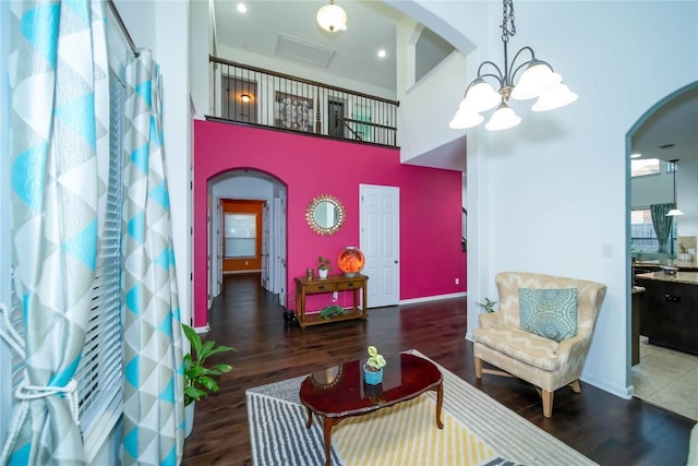 sitting room featuring arched walkways, a chandelier, wood finished floors, a towering ceiling, and baseboards