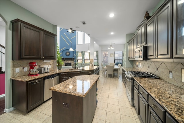 kitchen featuring stainless steel appliances, a sink, light stone counters, and a ceiling fan