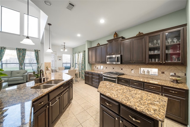 kitchen featuring tasteful backsplash, appliances with stainless steel finishes, a kitchen island, a sink, and dark brown cabinets