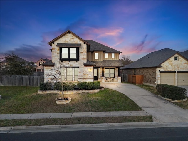 view of front of house featuring fence, stone siding, driveway, a lawn, and board and batten siding