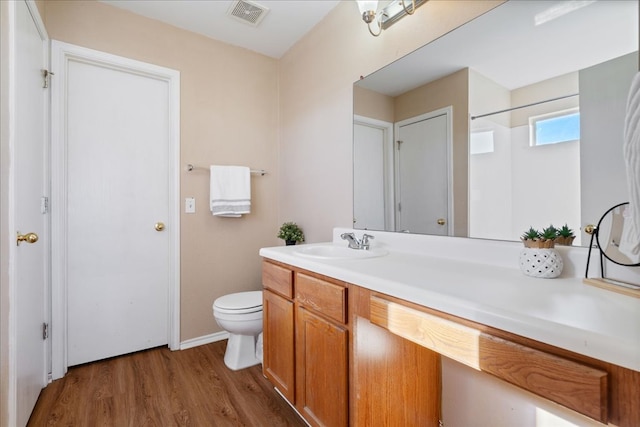 bathroom with toilet, vanity, wood finished floors, and visible vents