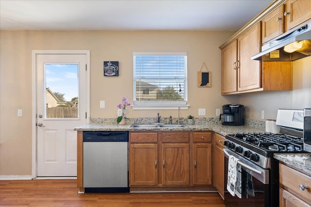 kitchen with under cabinet range hood, stainless steel appliances, a sink, light wood-style floors, and brown cabinets