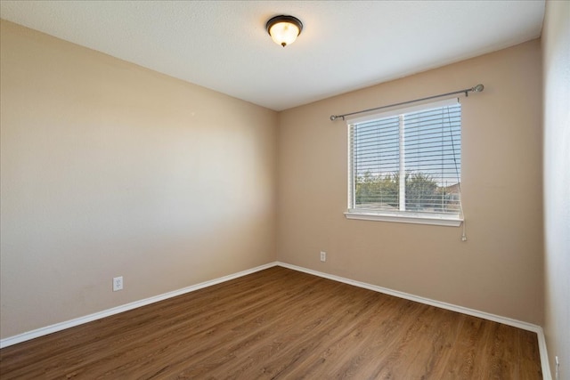 spare room with baseboards and wood finished floors