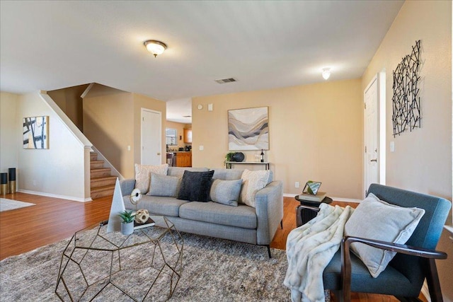 living room featuring stairs, visible vents, baseboards, and wood finished floors