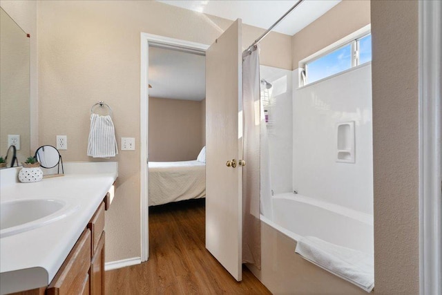 ensuite bathroom featuring baseboards, ensuite bath, wood finished floors, shower / bath combo with shower curtain, and vanity