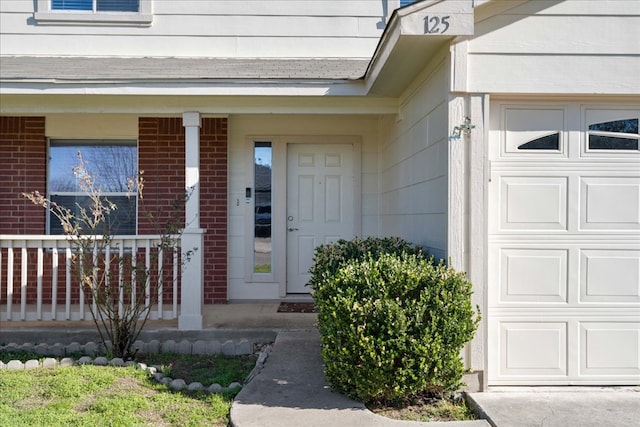 view of exterior entry featuring a garage, brick siding, and a porch