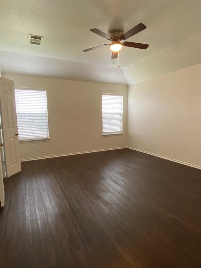 spare room with dark wood-style floors, vaulted ceiling, visible vents, and baseboards