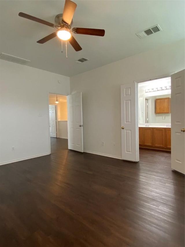 unfurnished bedroom featuring ensuite bath, visible vents, dark wood finished floors, and baseboards