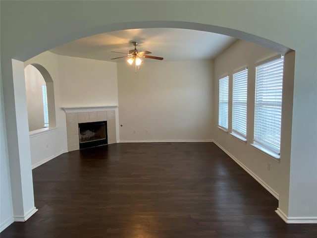 unfurnished living room featuring dark wood-style floors, ceiling fan, baseboards, and a tile fireplace