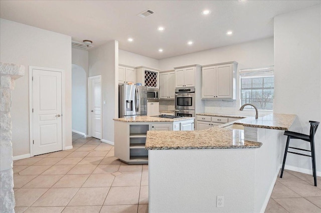 kitchen featuring visible vents, arched walkways, appliances with stainless steel finishes, light stone countertops, and a sink