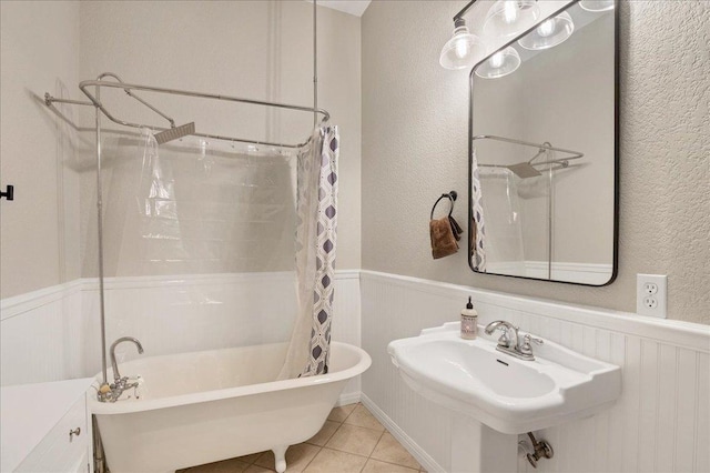 full bathroom featuring a wainscoted wall, a textured wall, shower / bathtub combination with curtain, a sink, and tile patterned flooring