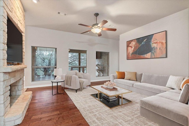 living area featuring ceiling fan, a fireplace, visible vents, baseboards, and wood-type flooring