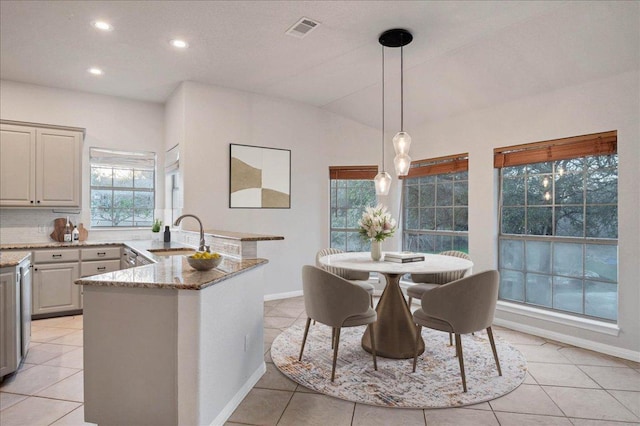 kitchen featuring light stone counters, a peninsula, a sink, visible vents, and hanging light fixtures