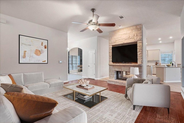 living room with arched walkways, a fireplace, visible vents, a textured ceiling, and wood finished floors