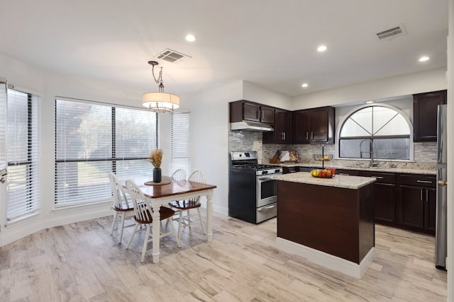 kitchen with stainless steel appliances, a sink, under cabinet range hood, backsplash, and a center island