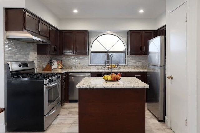 kitchen featuring stainless steel appliances, dark brown cabinets, light stone countertops, and under cabinet range hood