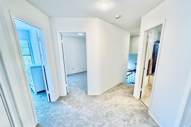 corridor featuring carpet, baseboards, and a textured ceiling