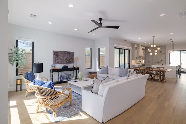 living room featuring light wood-type flooring, ceiling fan with notable chandelier, visible vents, and recessed lighting