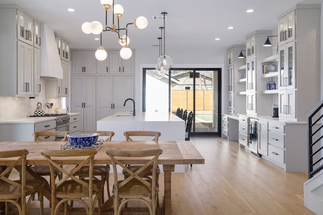 kitchen featuring light countertops, a center island with sink, premium range hood, and decorative backsplash