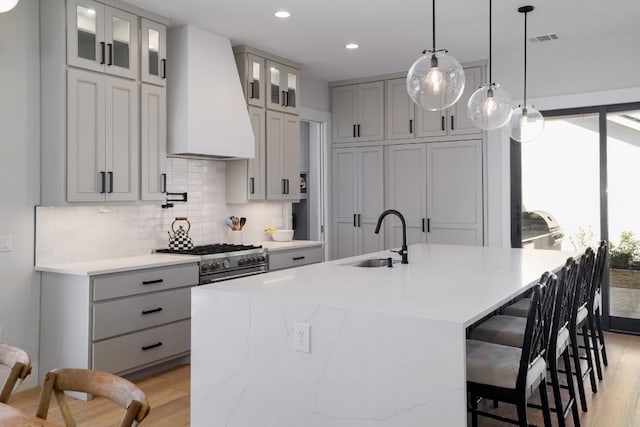 kitchen featuring visible vents, high end range, a sink, custom exhaust hood, and backsplash