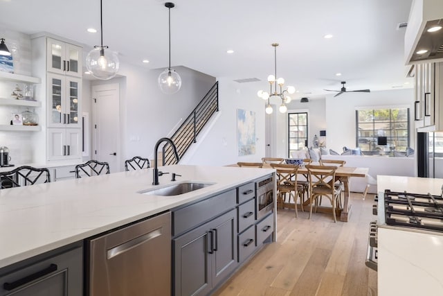 kitchen featuring pendant lighting, light wood finished floors, appliances with stainless steel finishes, white cabinets, and a sink