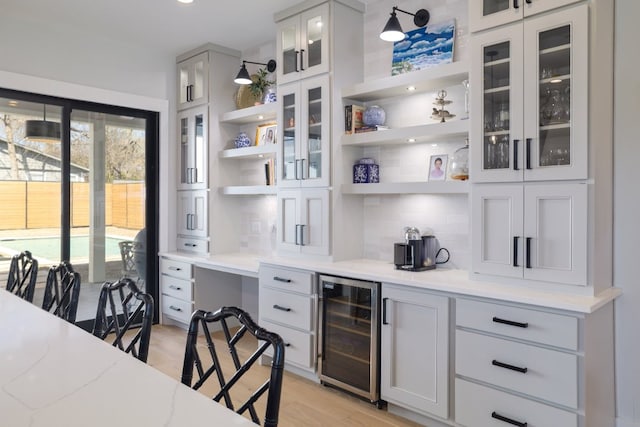 bar featuring beverage cooler, light wood-type flooring, backsplash, and built in study area