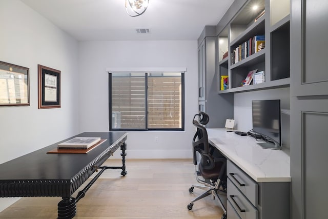 office with baseboards, visible vents, built in desk, and light wood finished floors