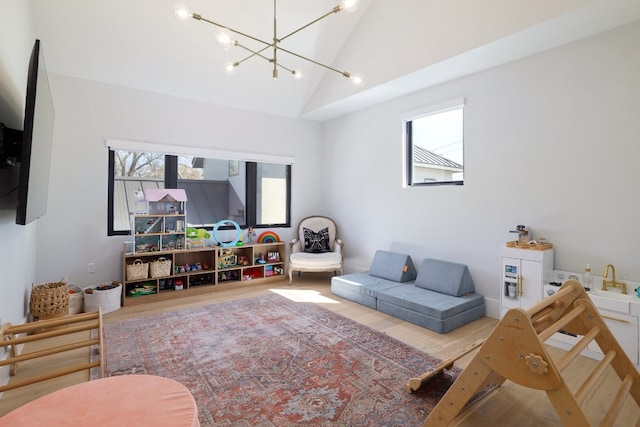 living area with high vaulted ceiling, a wealth of natural light, a notable chandelier, and wood finished floors