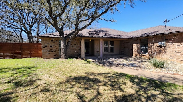 rear view of property featuring a yard, brick siding, and fence