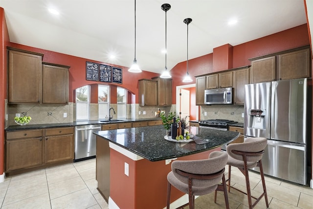 kitchen with light tile patterned floors, a breakfast bar area, a kitchen island, a sink, and appliances with stainless steel finishes