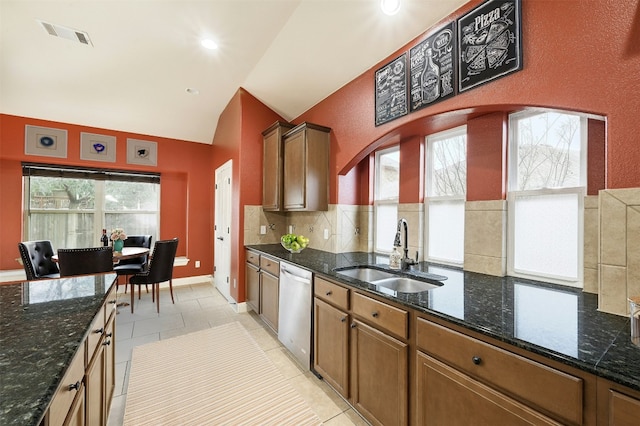 kitchen with a sink, vaulted ceiling, backsplash, dishwasher, and dark stone countertops