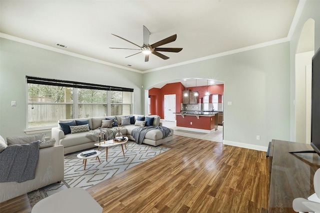 living room featuring arched walkways, crown molding, visible vents, light wood-style floors, and ceiling fan