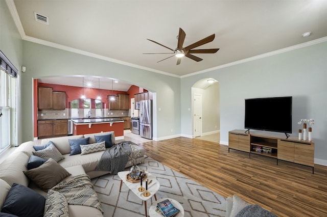 living area featuring arched walkways, ceiling fan, visible vents, baseboards, and light wood-type flooring