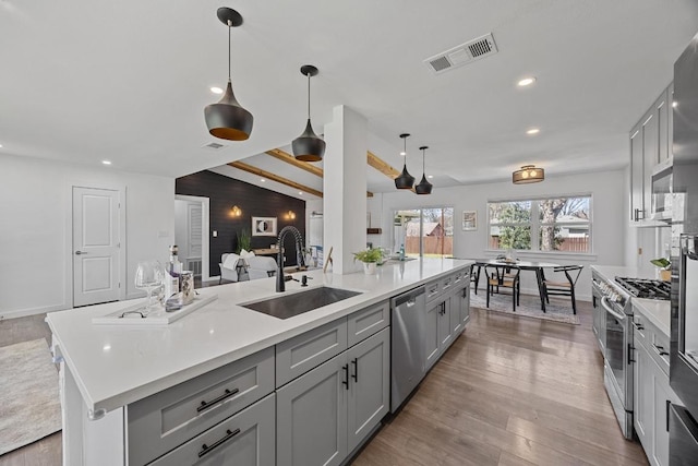 kitchen with gray cabinetry, wood finished floors, a sink, visible vents, and appliances with stainless steel finishes