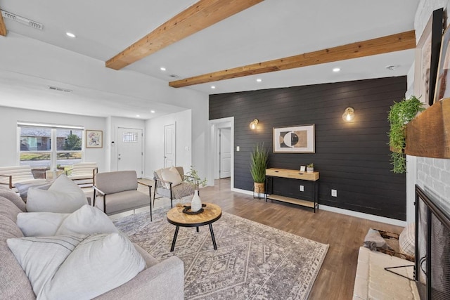 living room featuring visible vents, wood finished floors, a glass covered fireplace, and beam ceiling